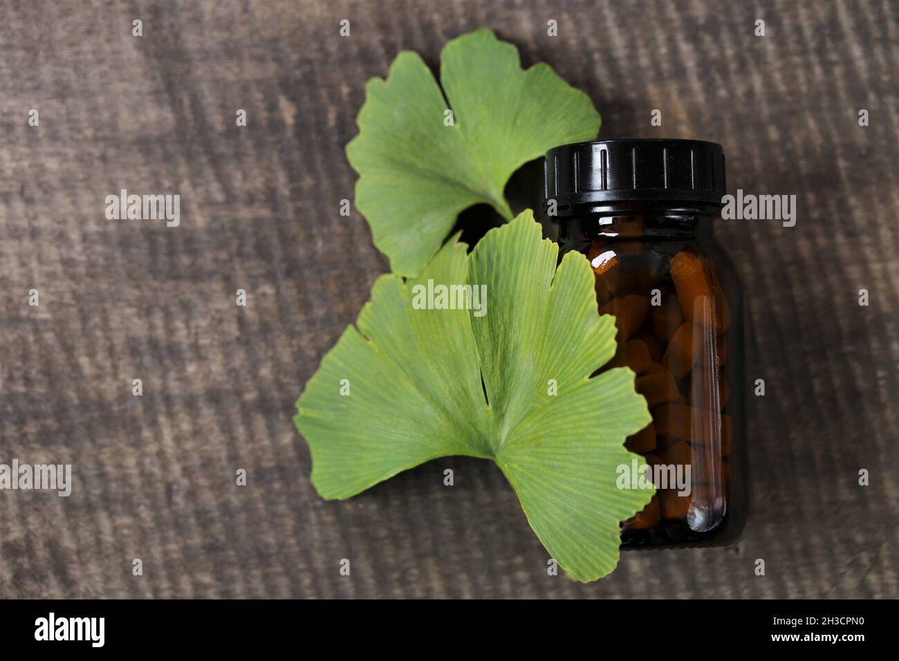 Ginkgo biloba Pillen.Braunes Glas mit homöopathischen Pillen mit Ginkgo-Extrakt und Ginkgo-Blätter auf hölzernen Hintergrund. Alternative Medizin und Stockfoto