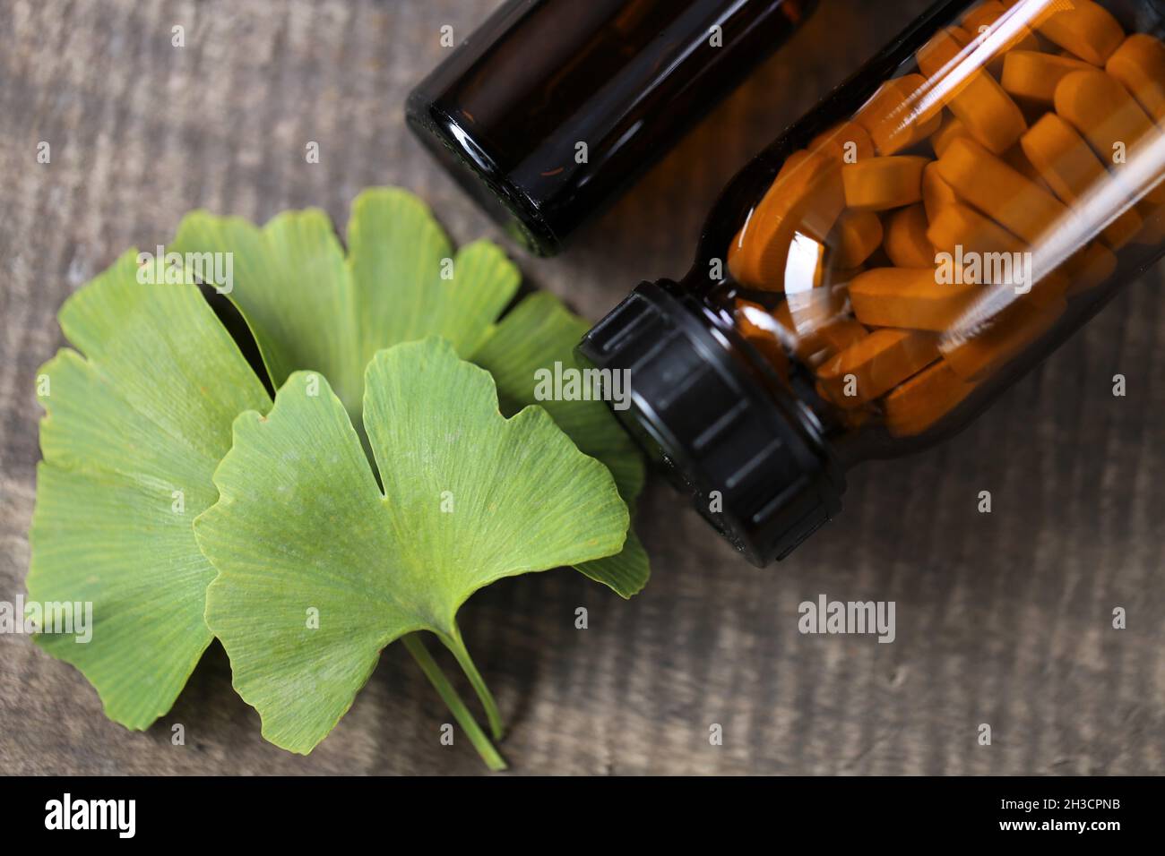 Ginkgo biloba Pillen.Braunes Glas mit homöopathischen Pillen mit Ginkgo-Extrakt und Ginkgo-Blätter auf hölzernen Hintergrund. Stockfoto