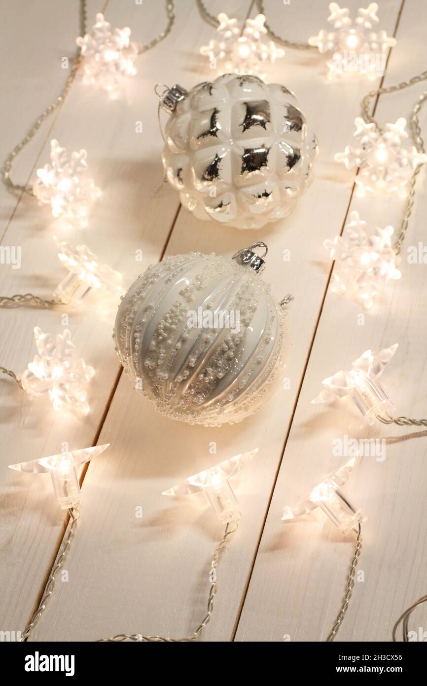 Weiß mit silbernen Weihnachtskugeln liegen auf einem weißen Holztisch zusammen mit einer leuchtenden Girlande. Blick von oben. Nahaufnahme Stockfoto