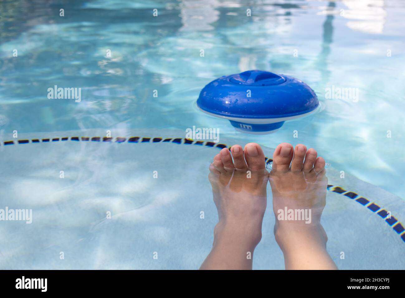 Weibliche Füße und blauer Kunststoff-Chlorspender im Wasser eines Schwimmbades. Stockfoto