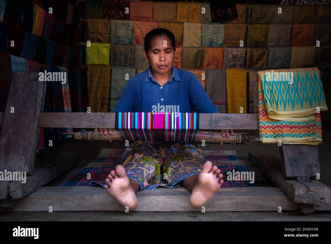 Eine Frau, die in West Nusa Tenggara, Indonesien, traditionelles Tuch mit traditionellem Werkzeug strickt Stockfoto