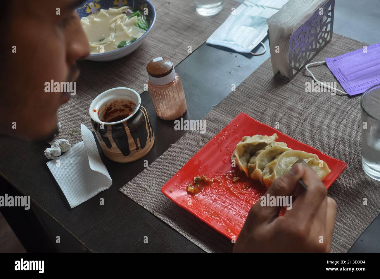 Rückansicht eines südasiatischen jungen Mannes, der im Fast-Food-Café Momos isst Stockfoto