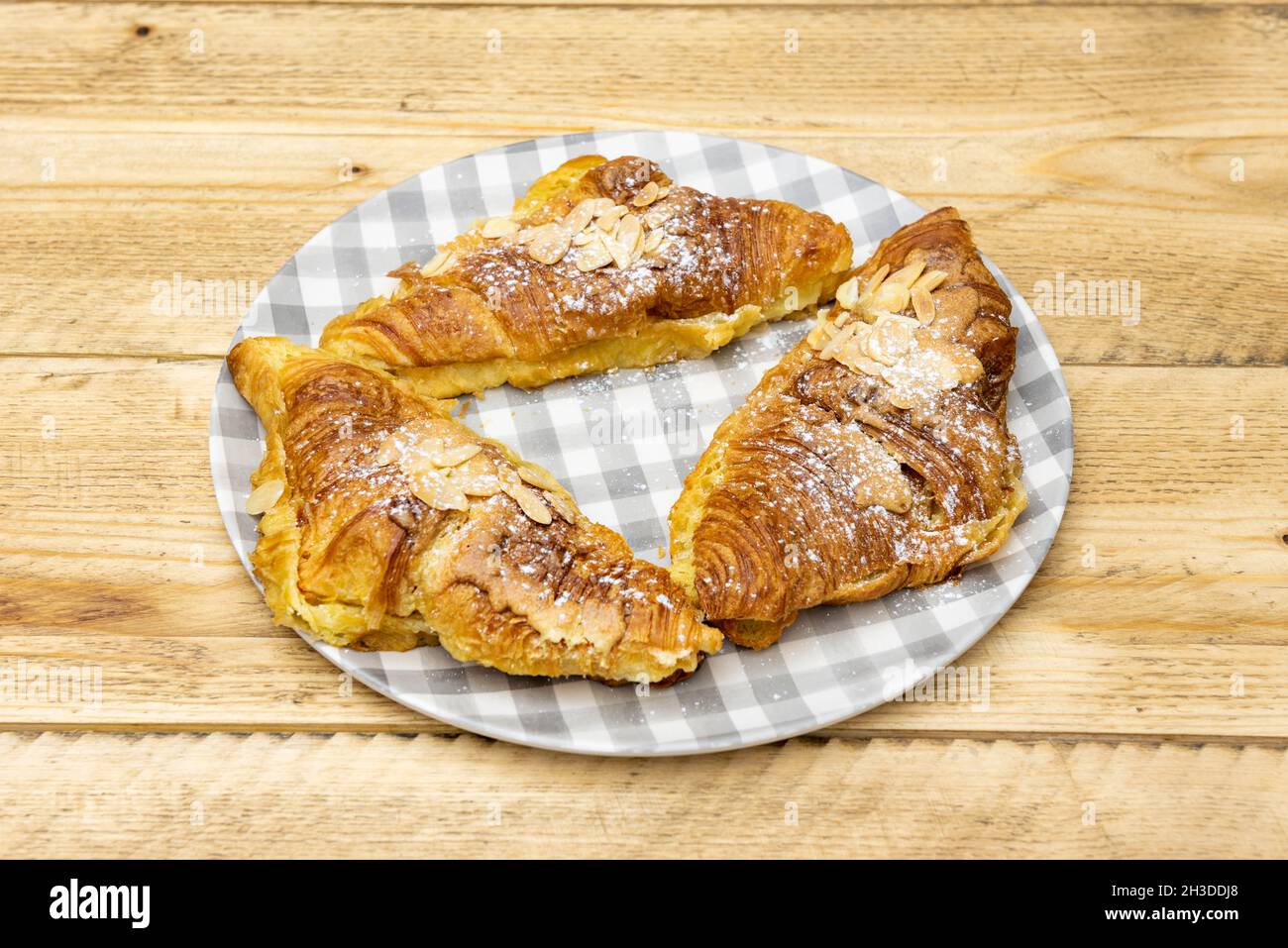 Leckere Buttercroissants mit Mandelscheiben, Sirup und Puderzucker auf rohem Holztisch Stockfoto