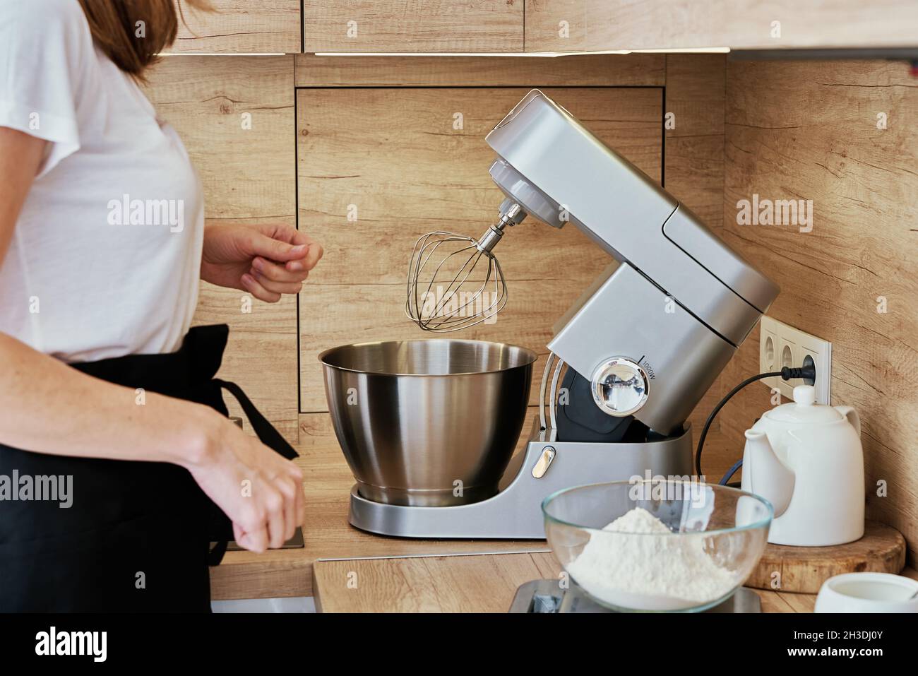 Frau kocht hausgemachten Kuchen. Elektrischer Mixer und Lebensmittelzutaten in der Küche. Küchengeräte Stockfoto