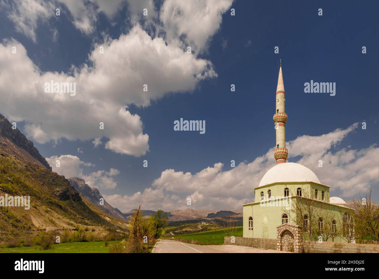 Straße hinauf zu den Nemrut Bergen mit muslimischer Moschee mit polychromem Minarett mit einem blauen Himmel voller Wolken und Lichtungen Stockfoto