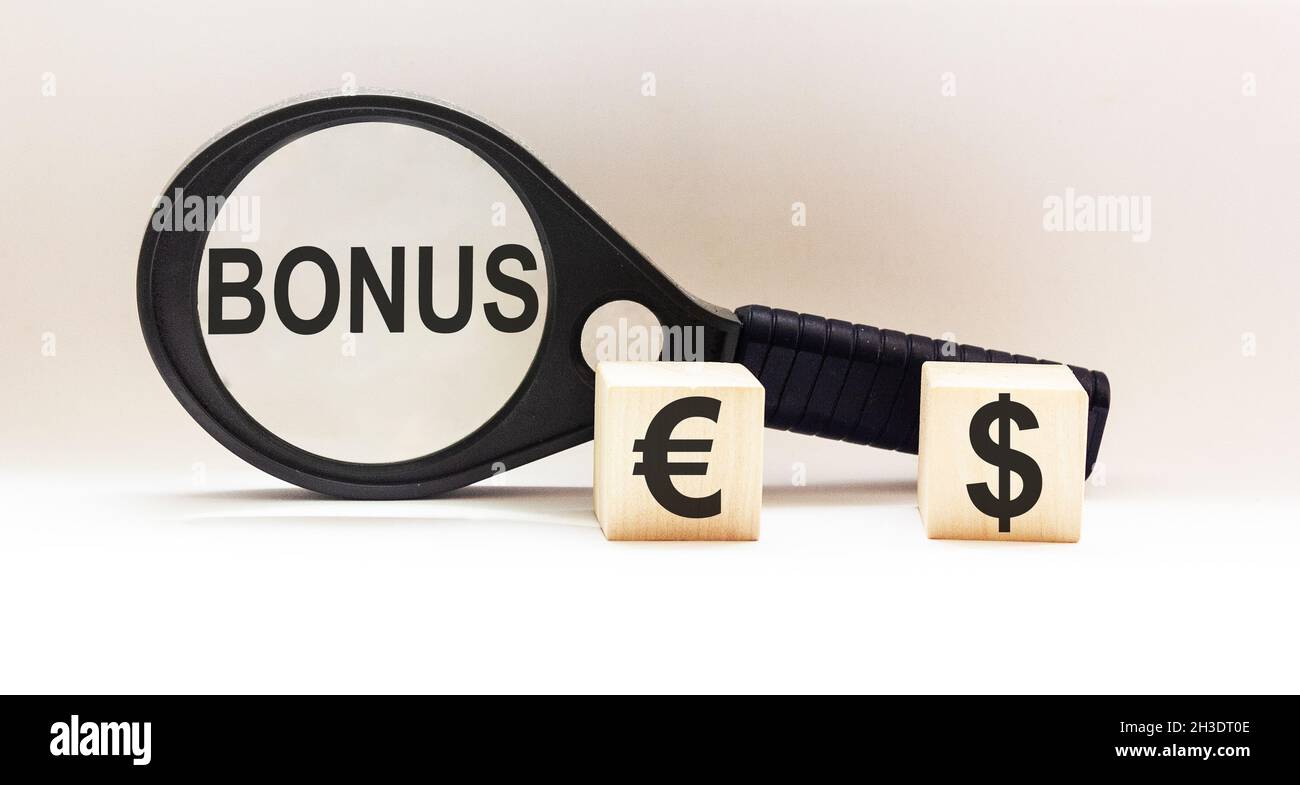 Das Wort BONUS ist auf einer Lupe geschrieben, mit Dollar- und Euro-Symbolen auf den Würfeln. Geschäftskonzept Stockfoto