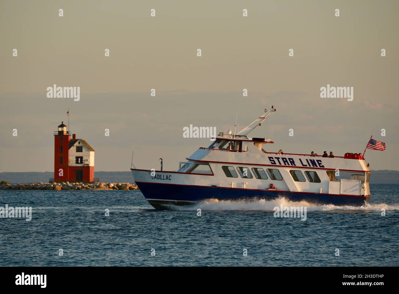 Fähre, die Touristen mit Round Island Lighthouse über die Meerenge von Mackinac Island im Hintergrund, Mackinac Island, Michigan, USA, transportiert Stockfoto