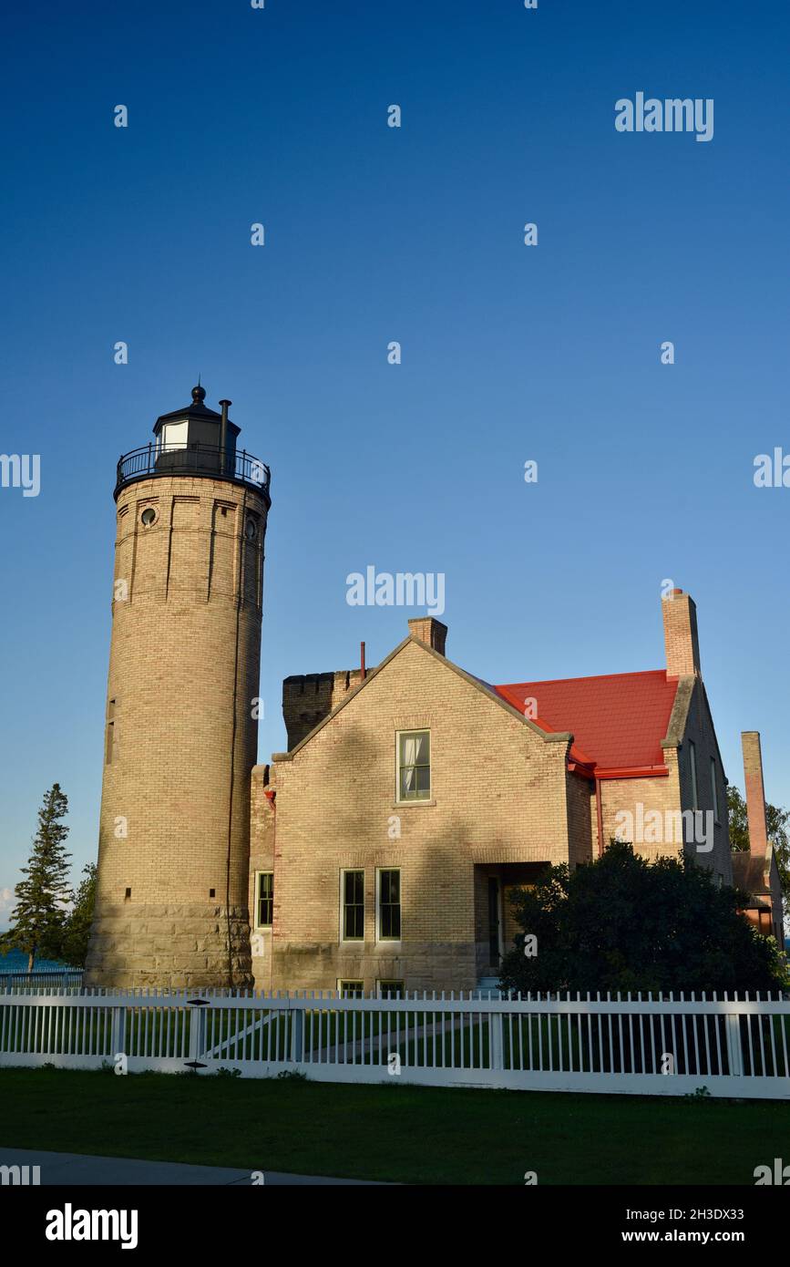 Historischer, aus Backstein gegangener Old Mackinac Point Lighthouse (1889), 'Castle of the Strait', weißer Zaun mit hellblauem Himmel, Mackinaw City, Michigan, USA Stockfoto