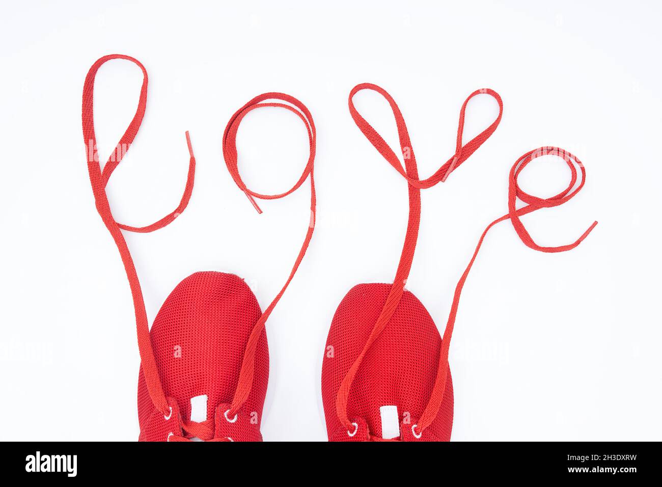 Crop-Ansicht der roten Sportschuhe und Schriftzug LOVE aus den Schnürsenkeln auf Weiß isoliert. Ich liebe es, ein kreatives Konzept zu entwickeln. Stockfoto