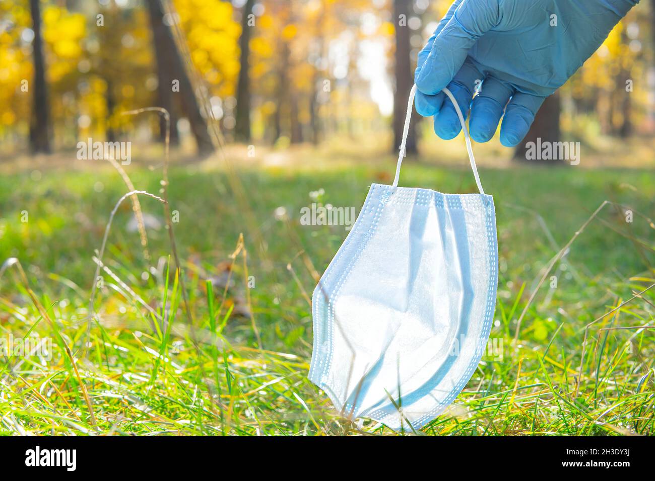 Nahaufnahme einer Hand, die einen Einweghandschuh trägt und eine weggeworfene einmal-Gesichtsmaske vom Boden im Stadtpark aufnimmt. Richtig sicher und umweltfreundlich Stockfoto