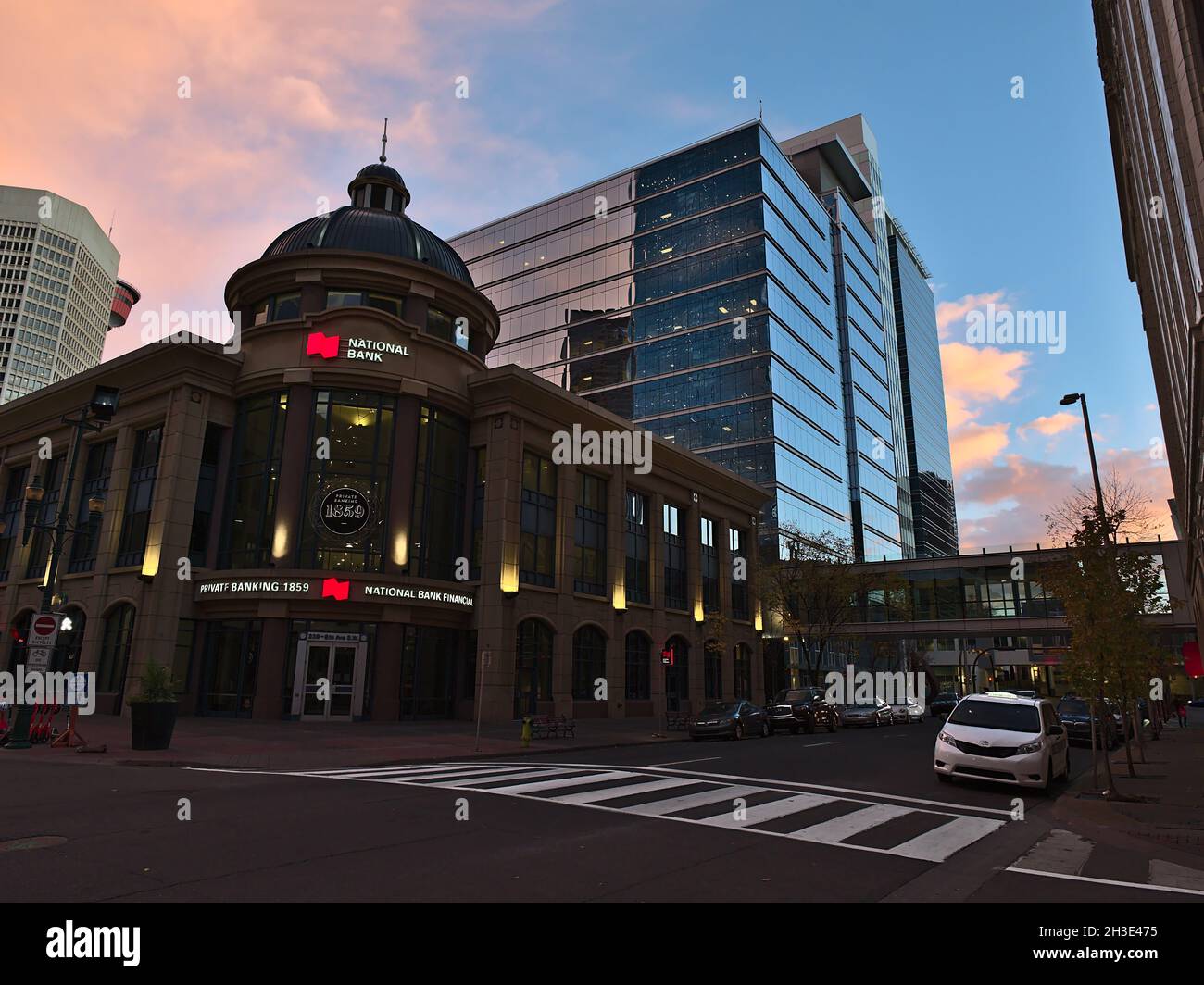Ansicht der Kreuzung von 2 St SW und 8 Ave SW im Stadtzentrum von Calgary mit einer Zweigstelle der National Bank of Canada (NBC) im Abendlicht mit rosa Himmel. Stockfoto