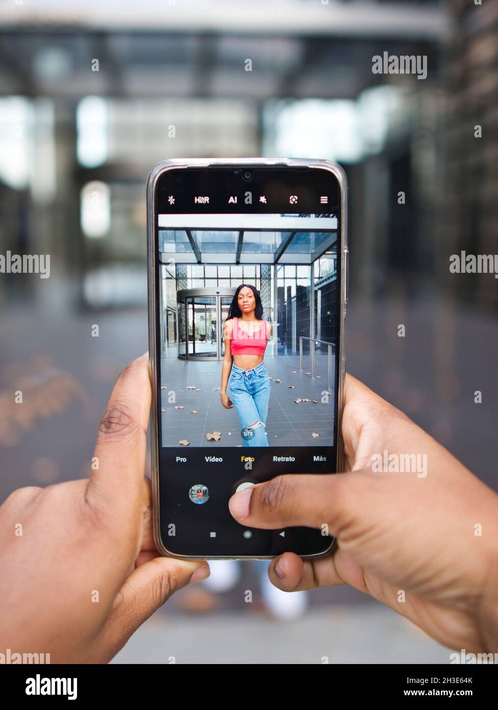 Crop anonyme Person, die Foto von afroamerikanischen Frau in stilvoller Kleidung auf dem Smartphone, während auf der Straße vor verschwommenem Hintergrund stehen Stockfoto
