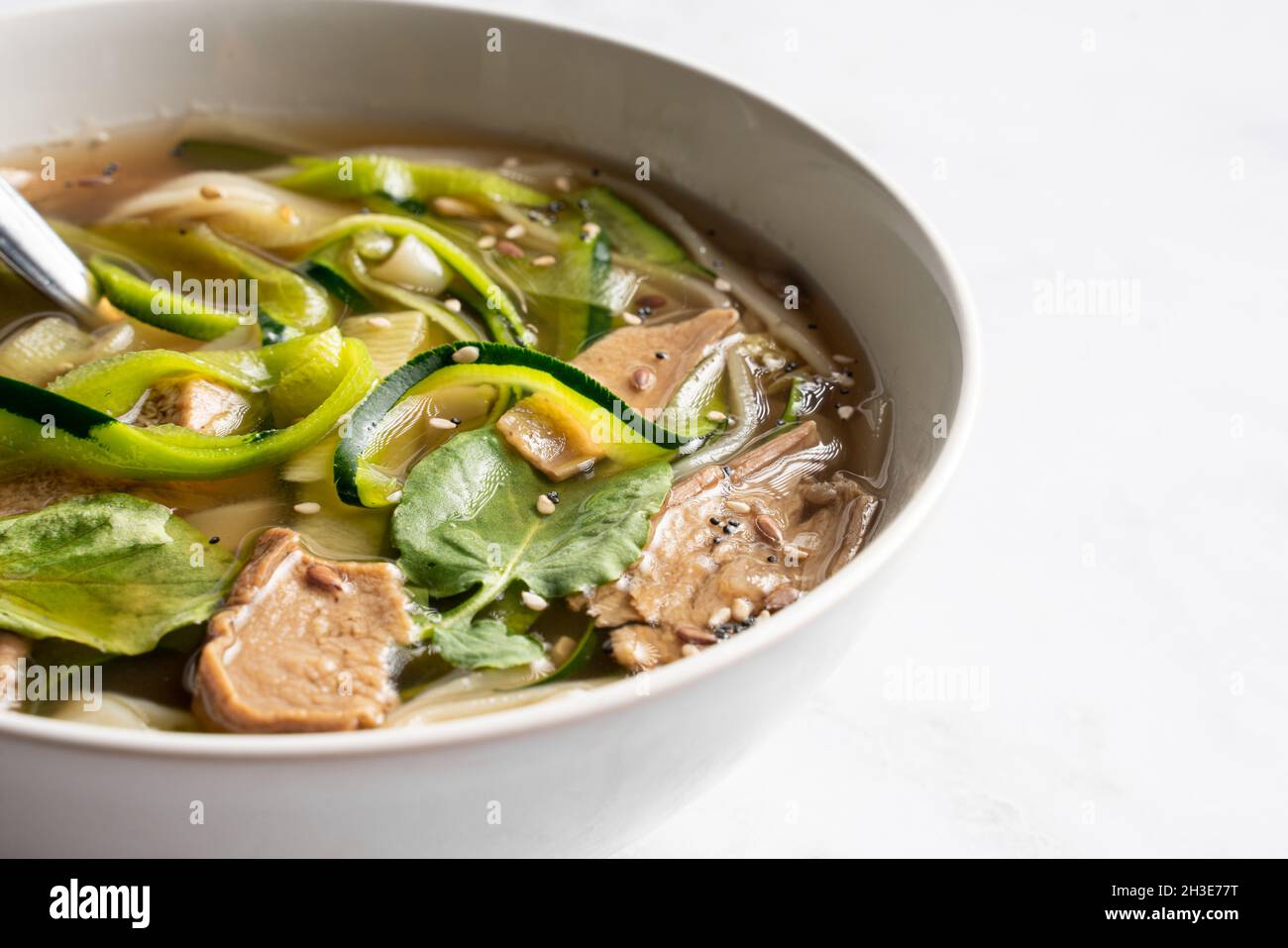 Schüssel mit traditioneller vietnamesischer Nudelsuppe Pho bo mit Basilikumblättern und Kalk auf Marmortisch im hellen Raum Stockfoto