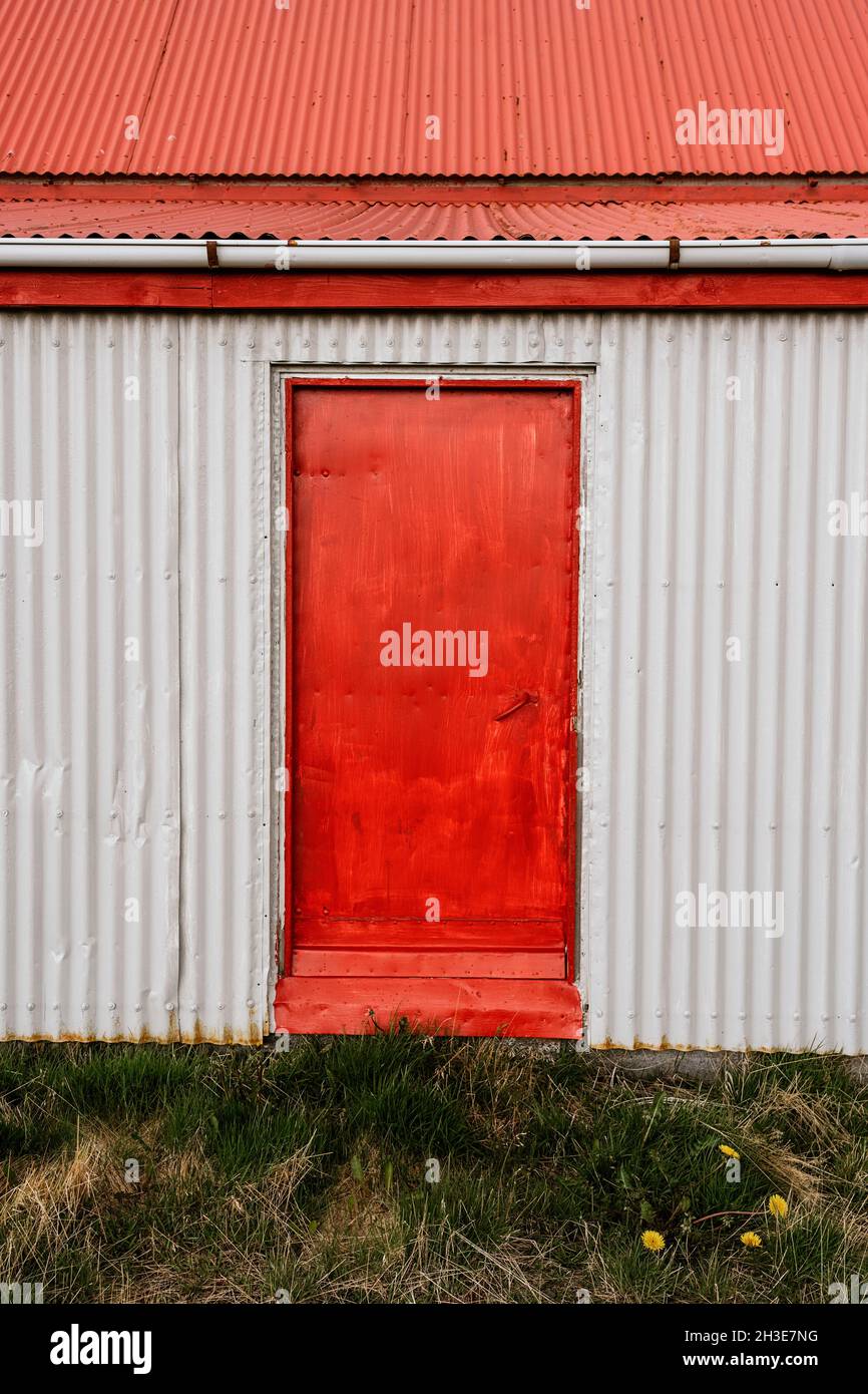 Fassade eines alten Metallhauses mit roter Tür und Dach auf einer Wiese in der Landschaft Stockfoto