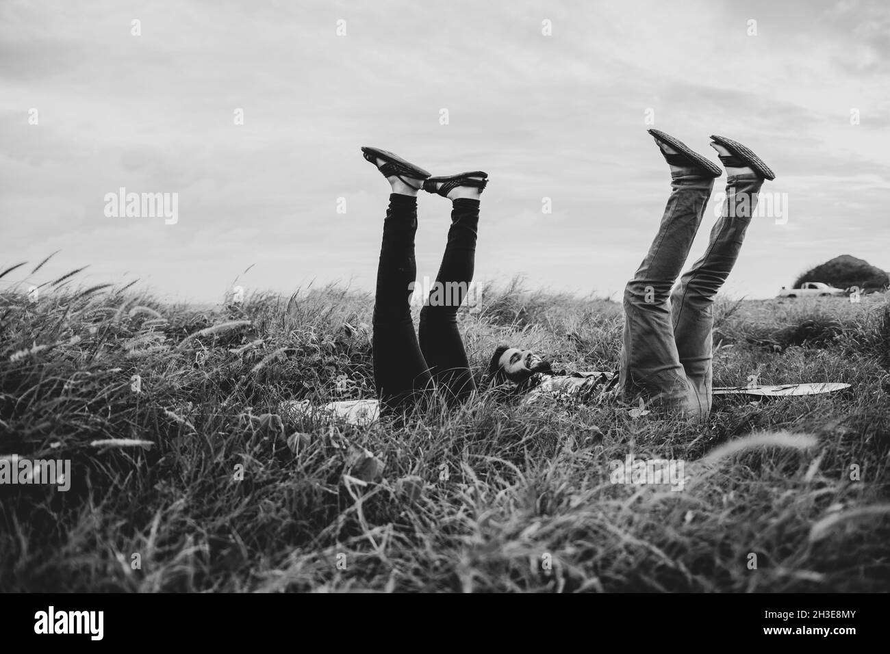 Schwarz und weiß von der Seitenansicht von fröhlichen Freunden in legerer Kleidung, die mit erhöhten Beinen auf grasbewachsenem Feld in der Natur bei Tageslicht liegt Stockfoto