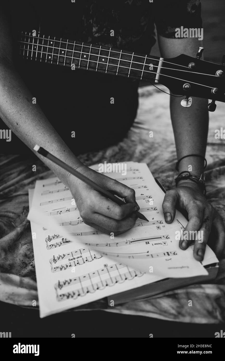Schwarz und weiß von Ernte unkenntlich männlichen Musiker sitzen mit Gitarre und Notizen in Noten bei Tageslicht Stockfoto