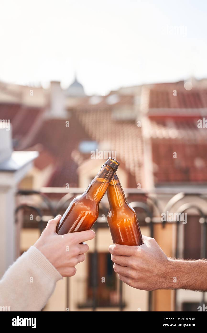 Unerkannte junge Freunde klirren Bierflaschen, während sie auf der Terrasse zusammen chillen Stockfoto