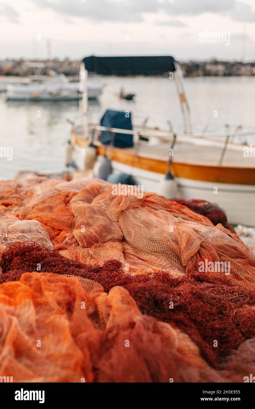 Farbenfrohe orangefarbene Fischernetze, die gegen ein modernes Boot gelegt werden, das bei Tageslicht im ruhigen Wasser des Meeres in der Nähe von Procida in Süditalien schwimmt Stockfoto