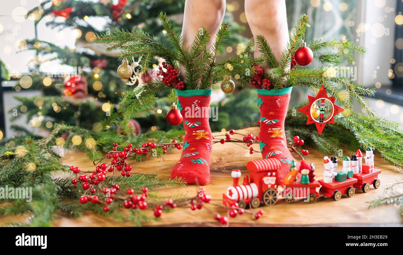 Verzierte Fichtenzweige werden auf den Füßen des Kindes in die Socken gesteckt. Roter Weihnachtszug als Innendekoration. Ein stimmungsvolles Weihnachtsfest Stockfoto