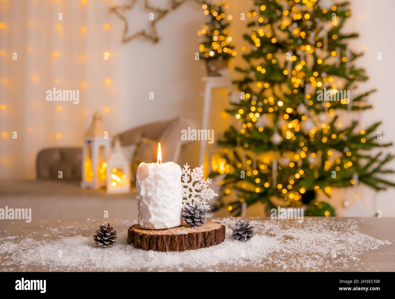 Selektiver Fokus auf das Kerzenbrennen von Schneeballmustern, dekoriert mit Pinienholzscheibe, weißer Schneeflocke-Dekoration und Kunstschnee auf dem Tisch. Stockfoto