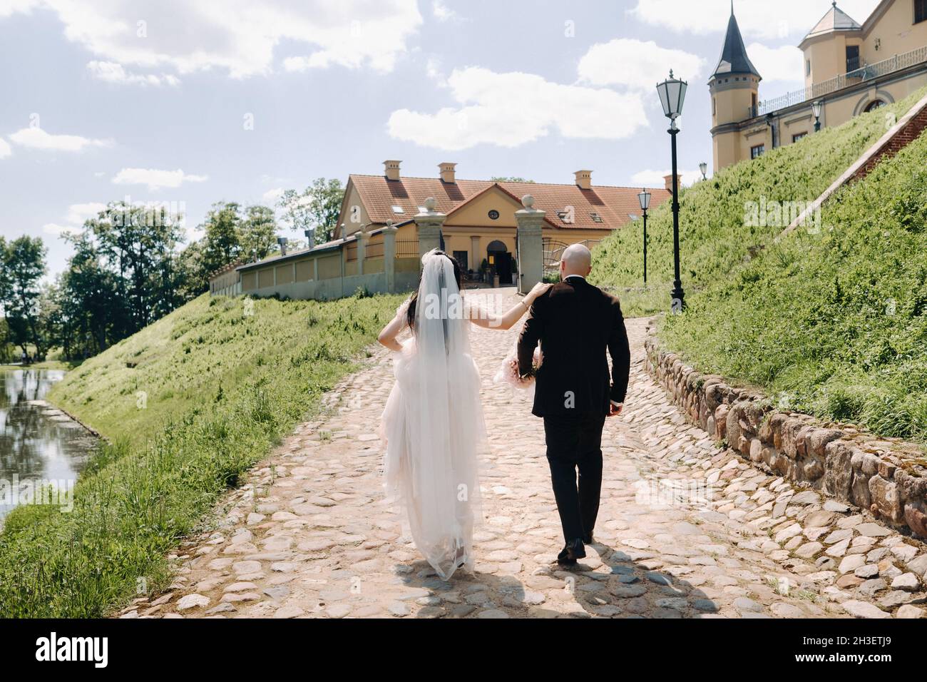 Rückansicht. Braut und Bräutigam gehen auf der Steinstraße in Richtung Schloss. Stockfoto