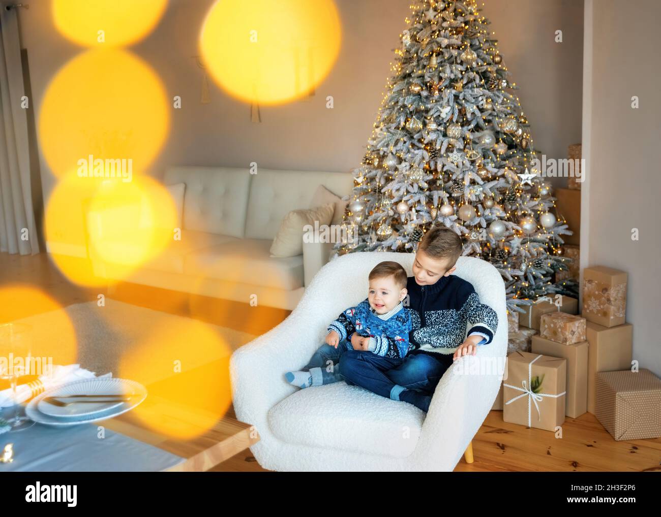 Liebevolle Brüder sitzen in der Nähe des Weihnachtsbaums mit vielen Geschenken. Frohes neues Jahr. Weihnachtsmorgen im hellen Wohnzimmer. Modisch wenig Stockfoto