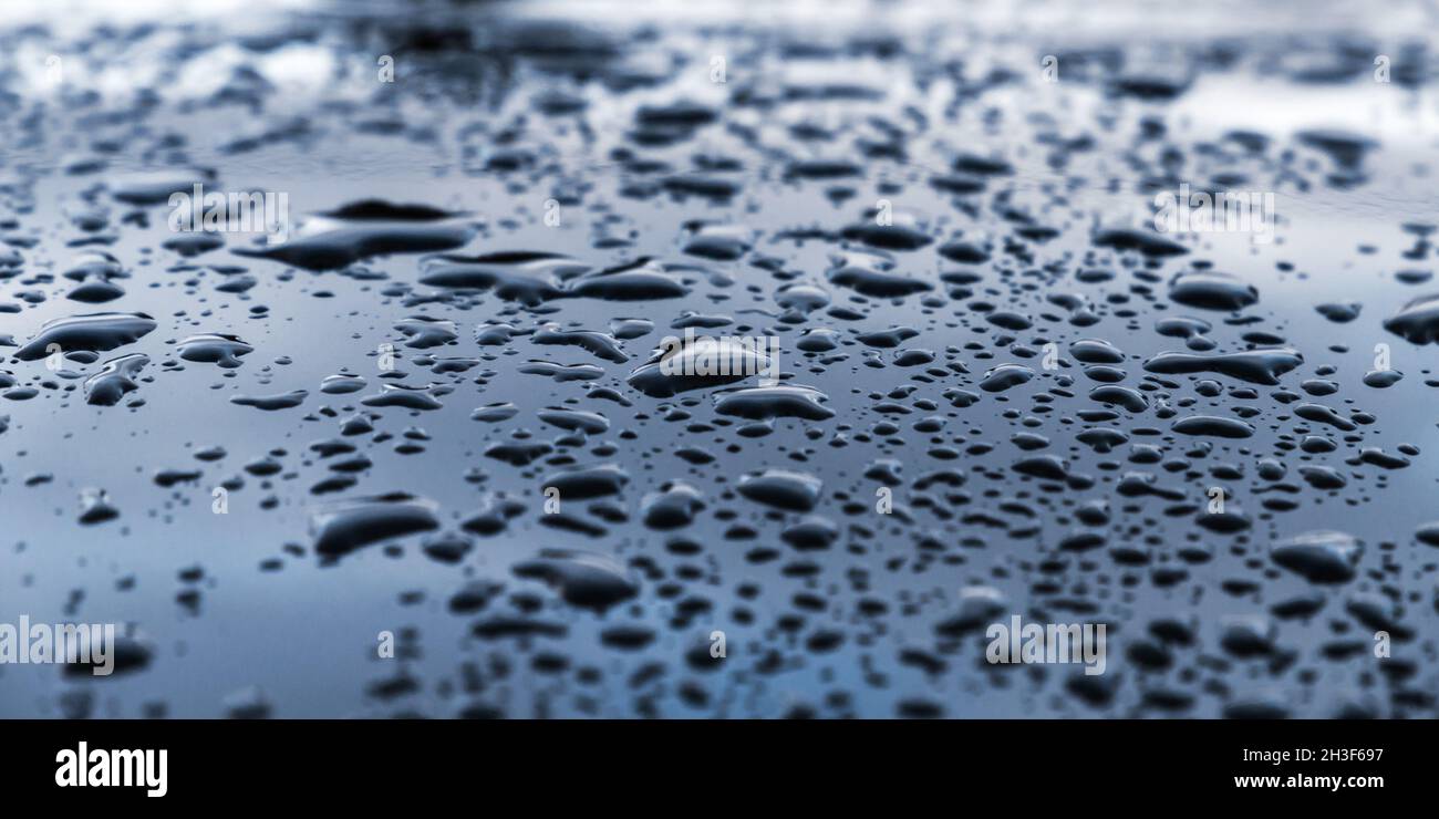 Glänzende schwarze Metallic-Motorhaubenoberfläche mit Wassertropfen darauf, Hintergrundbild mit selektivem Weichfokus Stockfoto