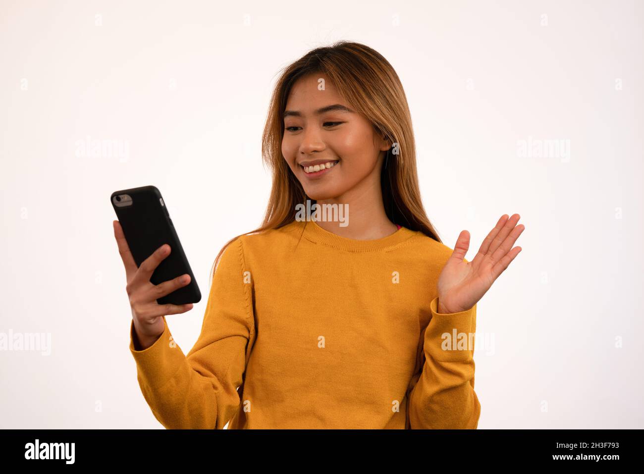 Junge attraktive asiatische Mädchen lächeln, während mit Smartphone im Studio Stockfoto