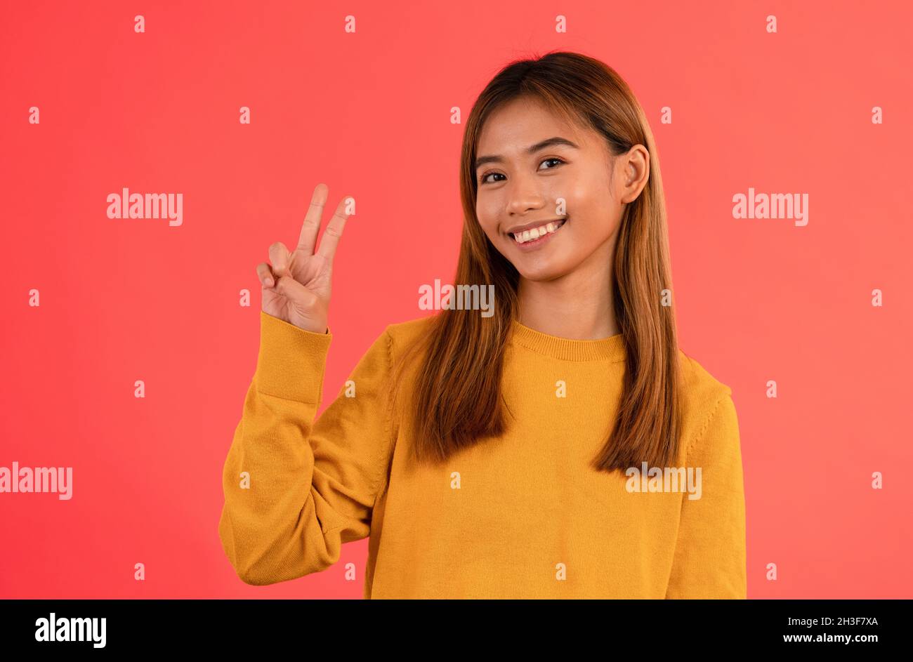 Junge attraktive asiatische Mädchen lächeln mit Frieden Zeichen im Studio Stockfoto