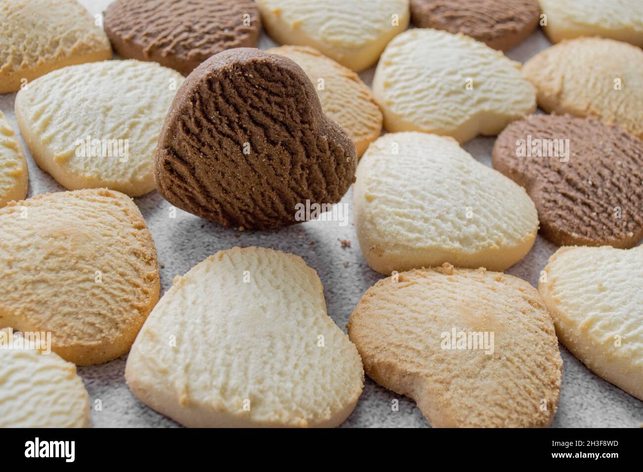 Viele bunte herzförmige Kekse auf einem Backblech, Schokolade am Rand. Stockfoto