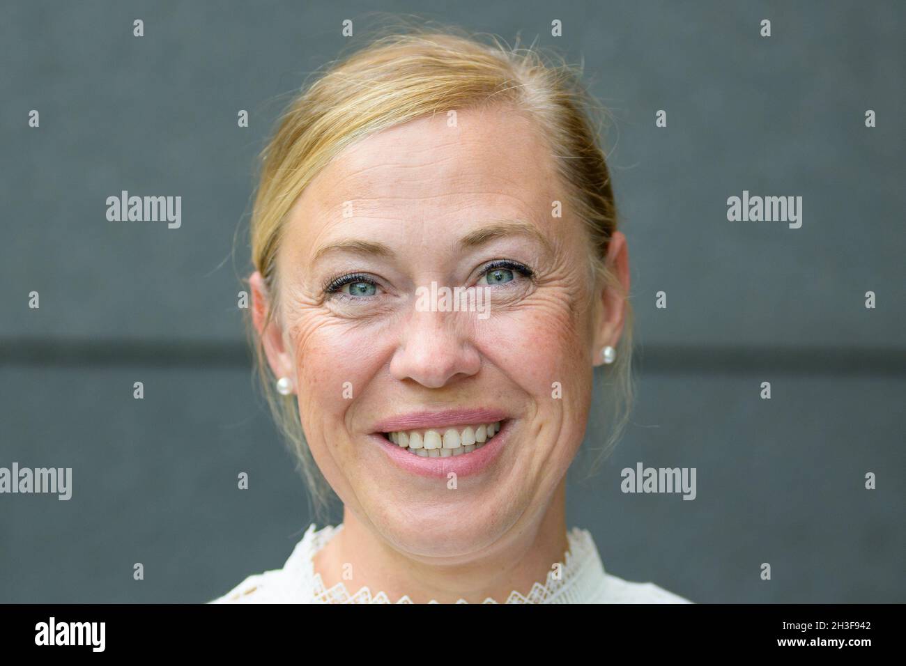 Nahaufnahme einer glücklich strahlenden blonden Frau mittleren Alters mit geöffneten Augen, die gegen eine graue Wand posiert Stockfoto
