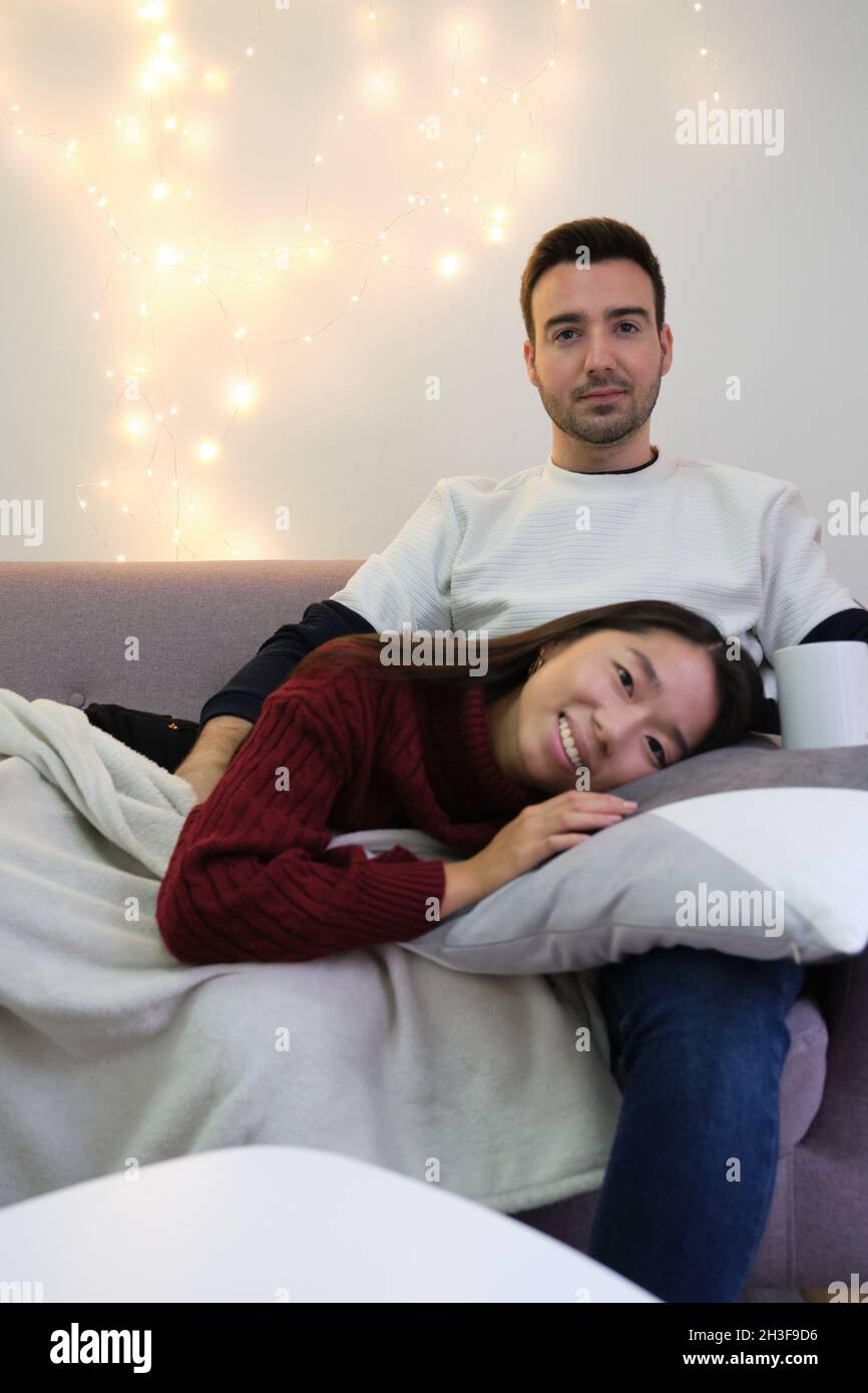 Junges Paar, das sich einen Weihnachtsfilm ansieht und auf dem Sofa sitzt und liegt. Stockfoto