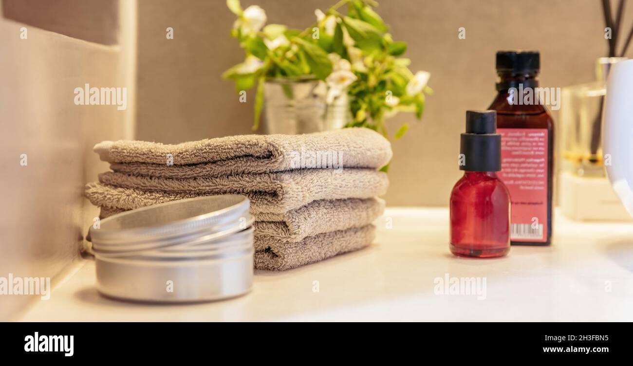 Flaschen und Handtücher aus ätherischem Öl auf dem Tisch gefaltet. Hausgemachte gesunde Naturprodukte für Körper- und Gesichtspflege. Moderne Spa-Innenausstattung. Stockfoto