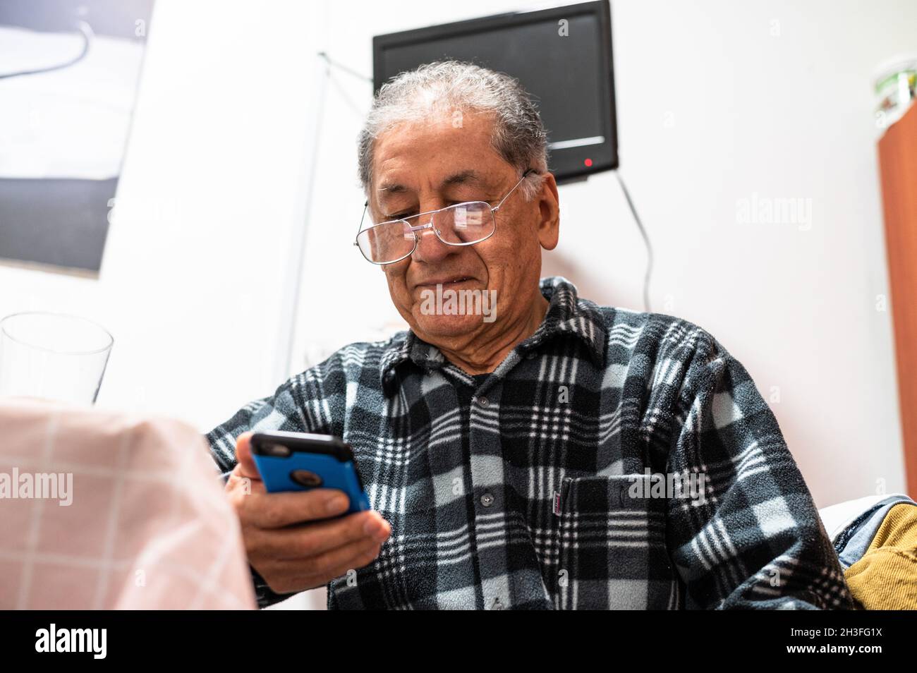 Glücklicher älterer kaukasischer Mann mit Brille schaut auf den Handybildschirm und stöbere im kabellosen Internet. Lächelnd moderne reife 70er Jahre Großvater Text oder Nachricht auf dem Smartphone. Ältere Menschen nutzen zu Hause Zelltechnologien. Stockfoto