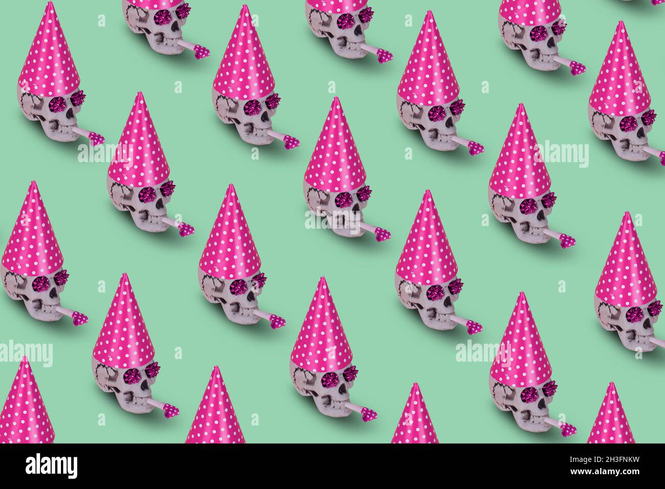 Muster aus menschlichem Schädel mit rosa Geburtstagsmütze und Pfeife auf grünem Hintergrund. Minimale Feiertagsfeier lustiges Konzept. Halloween kreativ zurück Stockfoto