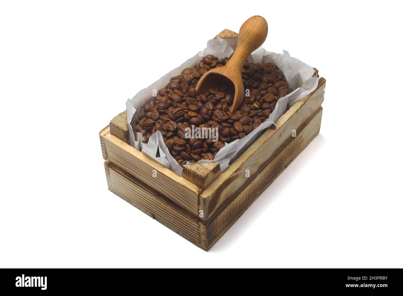 Nahaufnahme von gerösteten Kaffeebohnen in einer kleinen Holzkiste, isoliert auf weißem Hintergrund. Mit Holzlöffel. Stockfoto