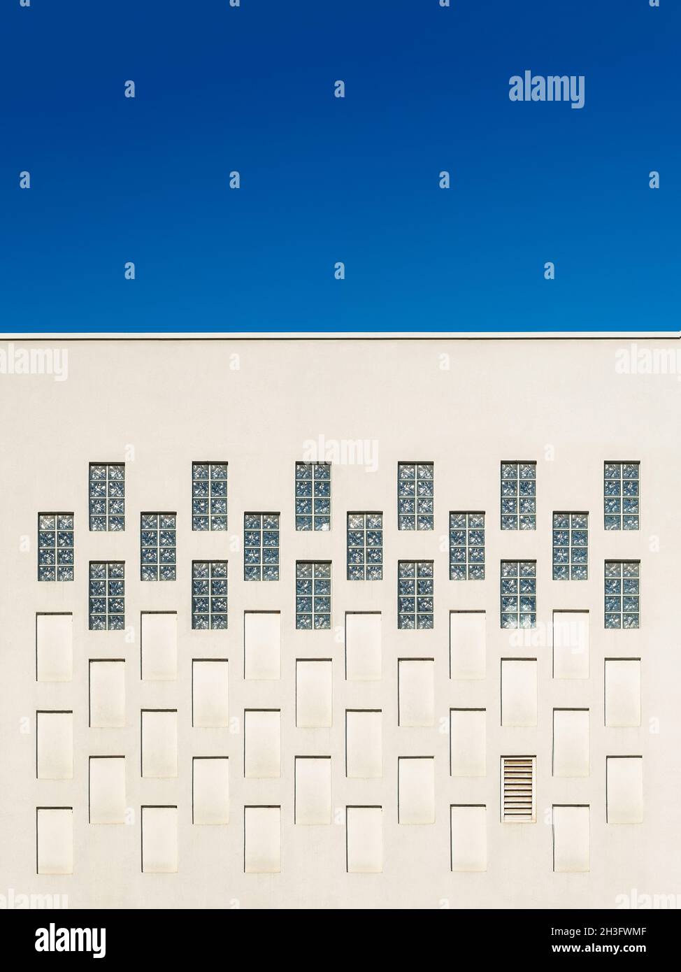 Rechteckige Fenster und Nischen in der äußeren Gebäudewand gegen blauen Himmel. Architektonische Elemente wiederholen Muster der modernen gebauten Struktur. Stockfoto