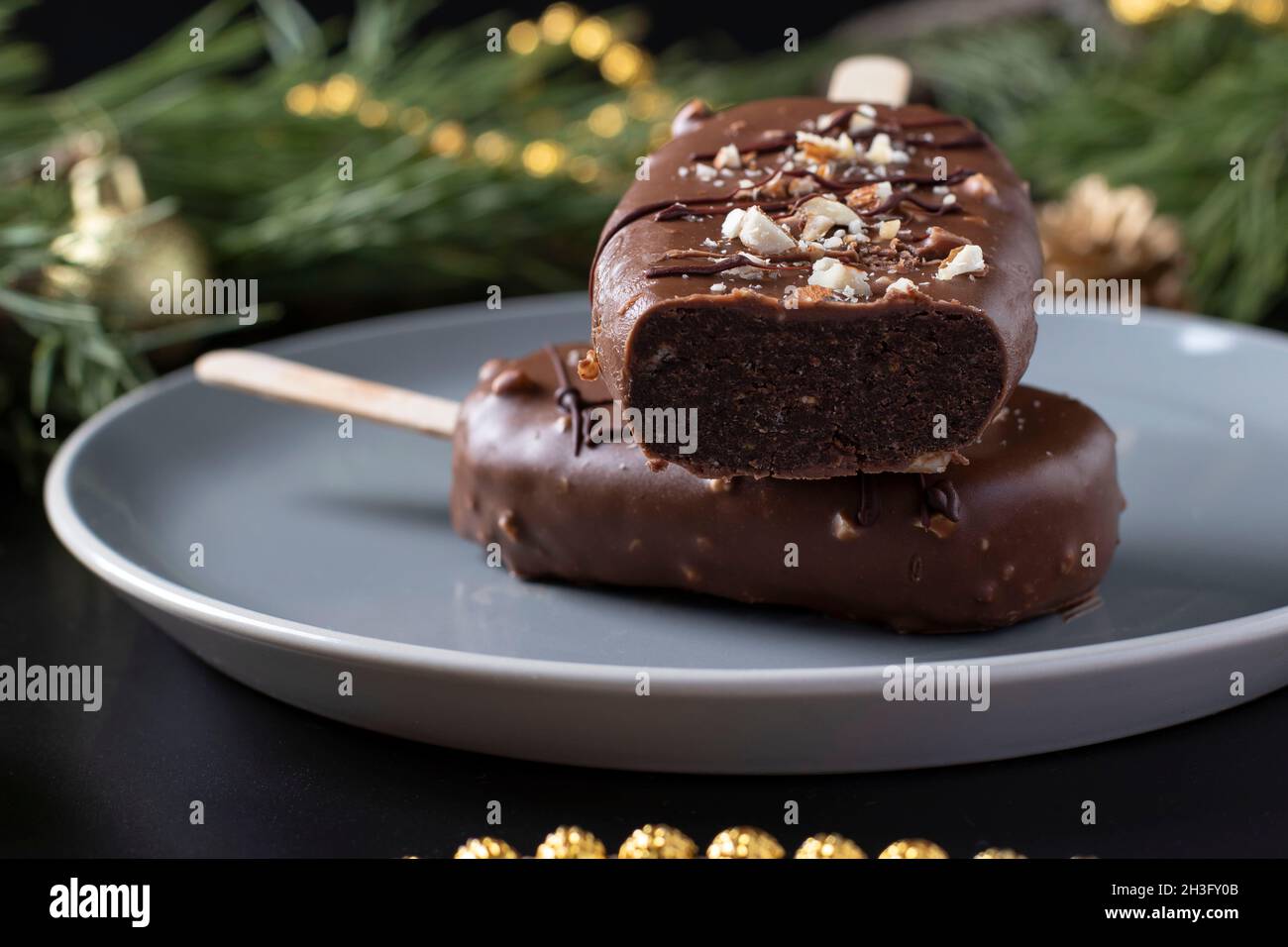 Schokoladen-Popsicle-Kuchen mit Nüssen auf einem Stock auf dunklem Hintergrund. Nahaufnahme Stockfoto