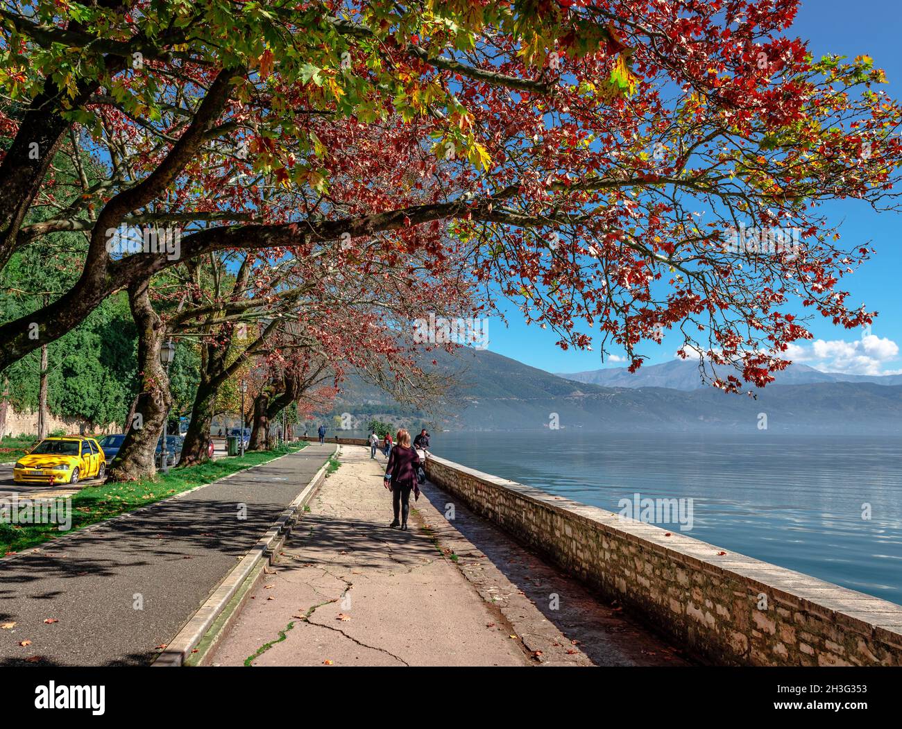 Ioannina, Griechenland - 22 2021. Oktober: Die Menschen gehen am Wasser spazieren und genießen einen sonnigen Tag im Herbst. Stockfoto