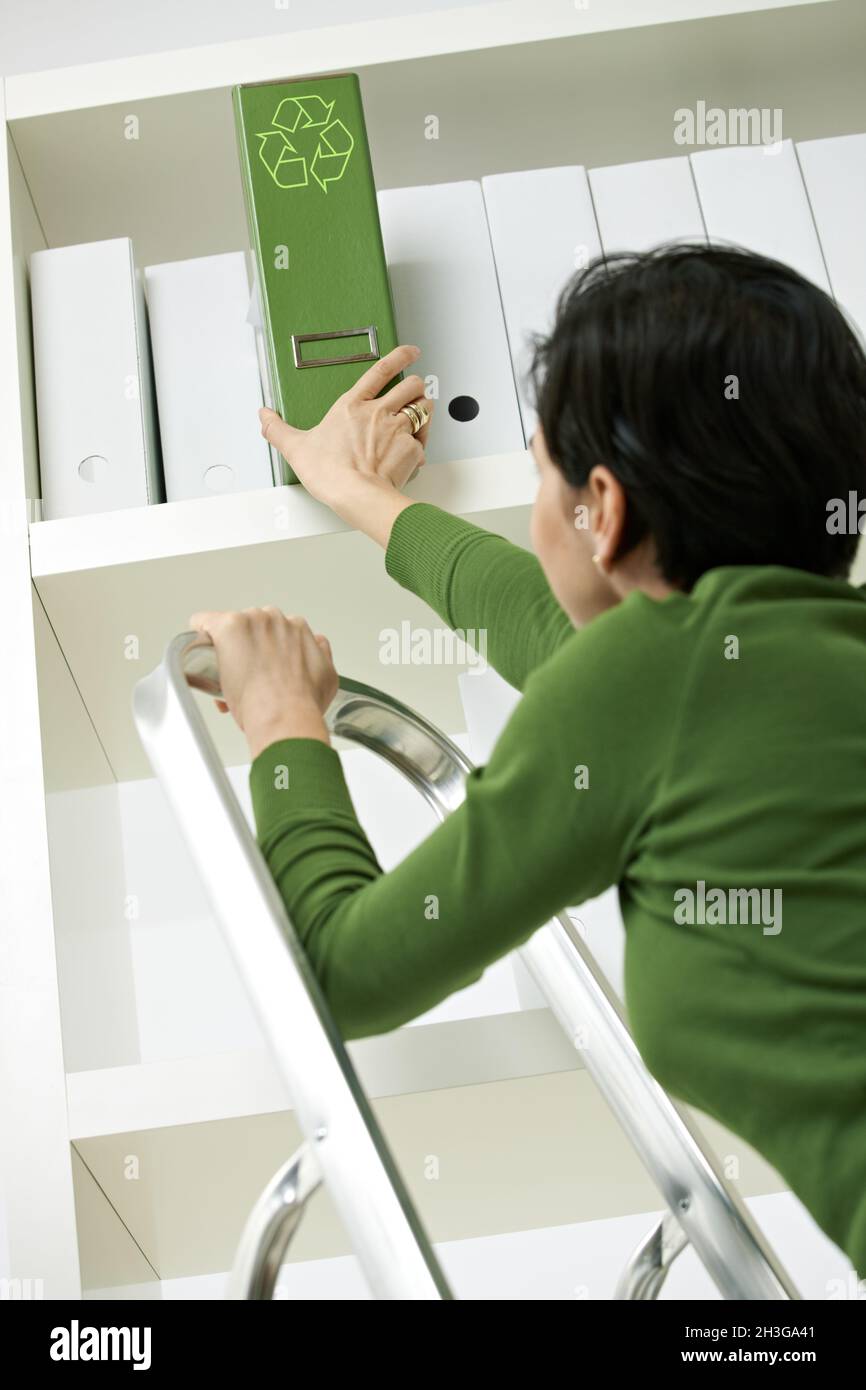 Frau entfernt grünen Ordner aus dem Regal Stockfoto