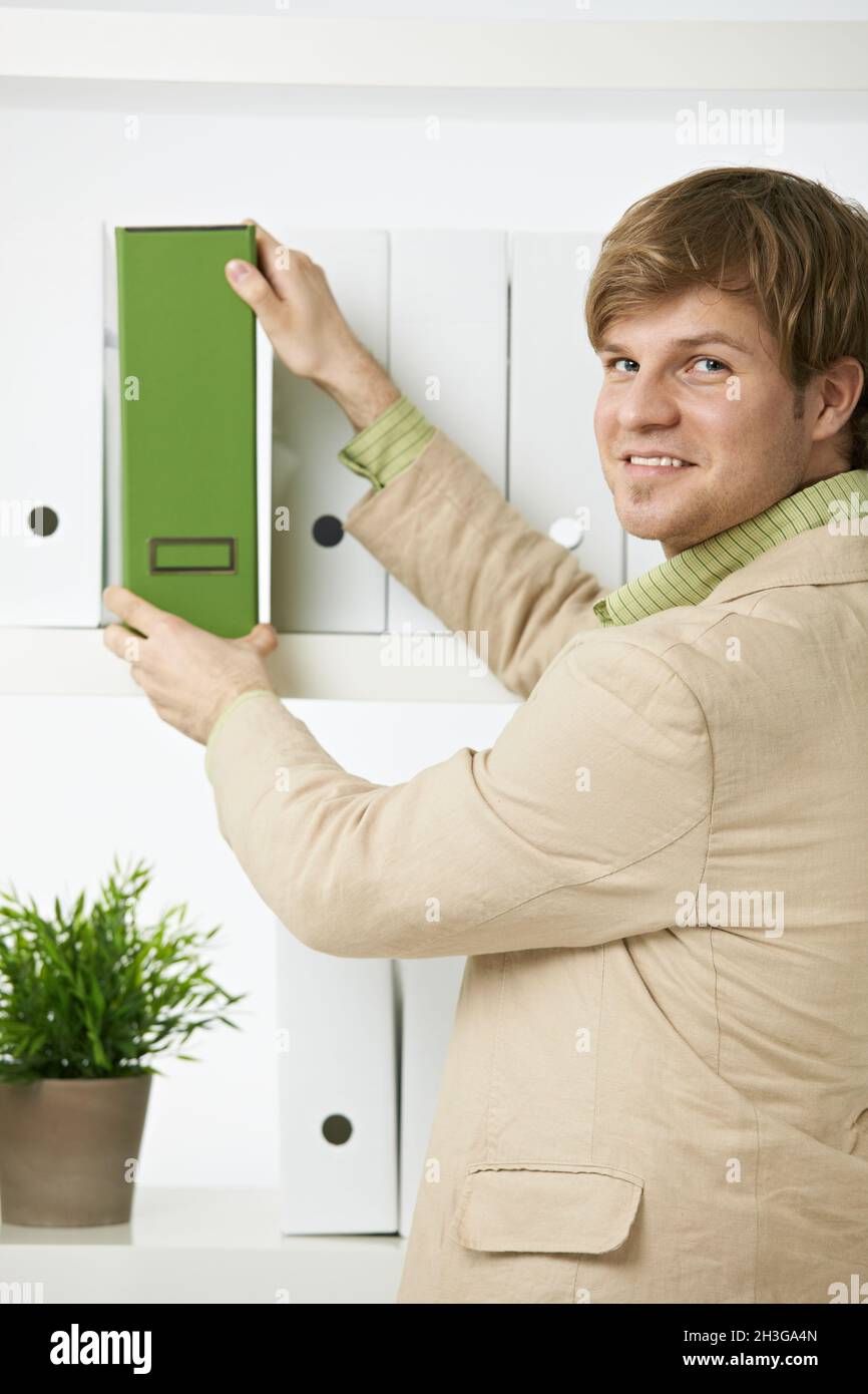 Geschäftsmann entfernt grünen Ordner aus dem Regal Stockfoto