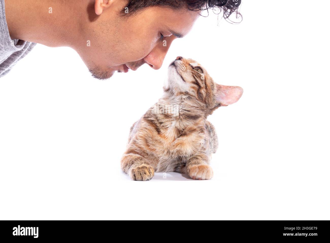 Gesicht des Mannes in der Nähe seiner Katze, isoliert auf weißem Hintergrund. Junger Erwachsener, der sein Haustier küssen will. Katze riecht ihren Besitzer. Stockfoto