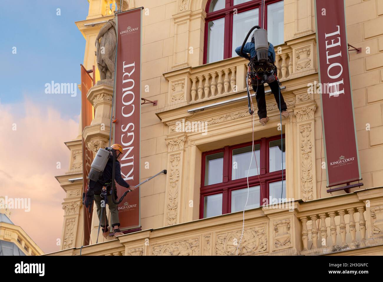 Prag, CZ - 28. oktober 2021:zwei Arbeiter mit Staubsaugern, die hoch oben auf der Rupe hängen und Staub an der Fassade eines Hotels in Prag reinigen. Sauber Stockfoto
