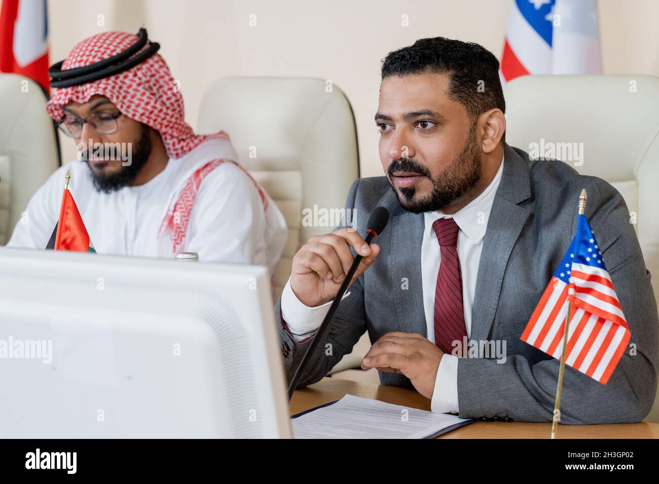 Politiker aus dem Nahen Osten sitzen mit Nationalflaggen am Tisch und nehmen an der Diskussion auf der Nationalkonferenz Teil Stockfoto