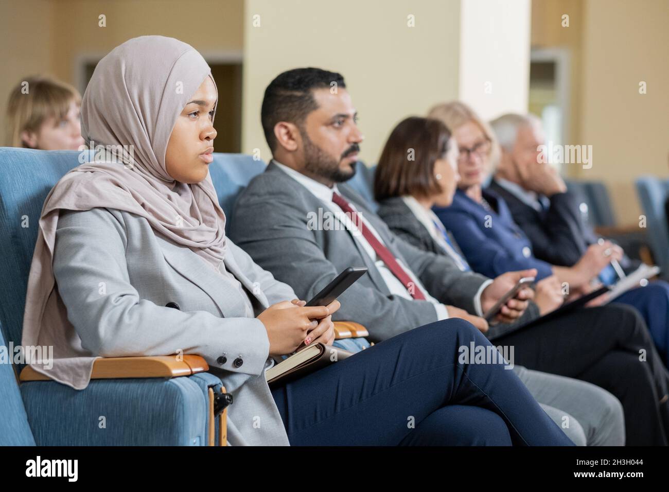 Eine Gruppe von seriös multiethnischen Geschäftsleuten, die im Auditorium sitzen und der Präsentation auf der Konferenz zuhören Stockfoto