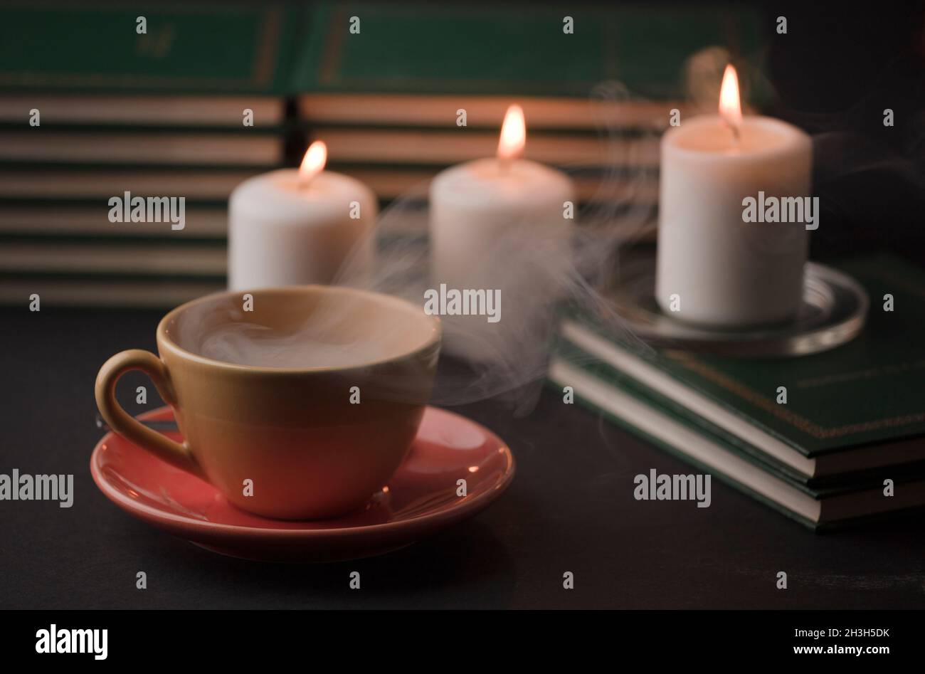 tasse Tee mit heißem Rauch und brennender Kerze. Auf dem Schreibtisch zu Hause, Stromausfall (Fokus auf Tasse). Stockfoto