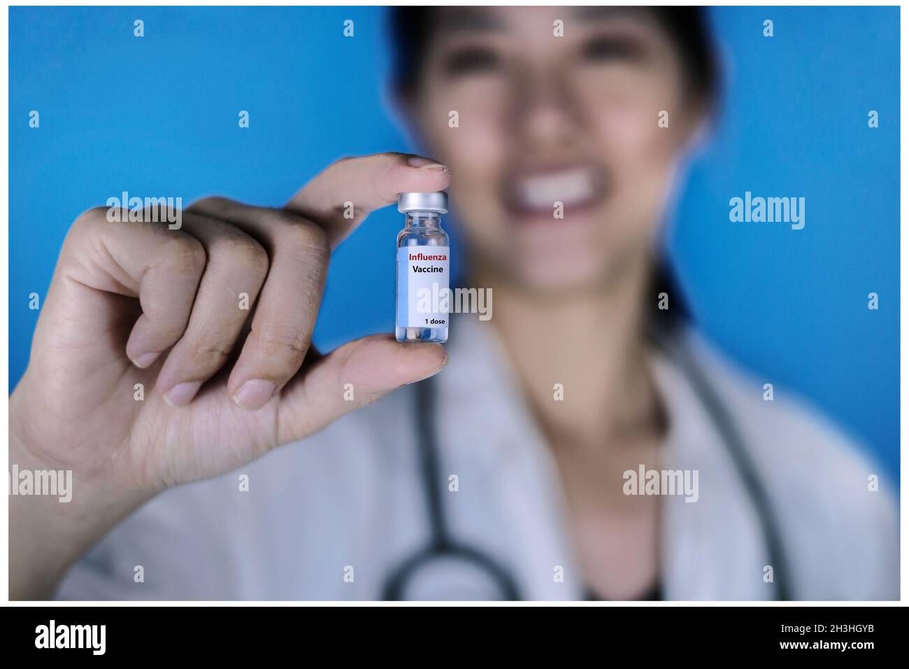 Eine Ärztin, die einen weißen Mantel mit einem Stethoskop um den Hals trägt und eine Glasfläschchen mit Influenza-Impfstoff oder einer mit den Fingern geschossenen Grippe hält, Smili Stockfoto