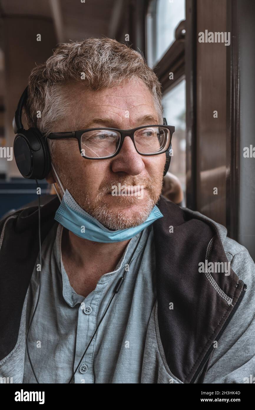 Porträt eines erwachsenen Mannes, der Kopfhörer und Brille mit einer medizinischen Schutzmaske am Kinn trägt. Unsachgemäße Verwendung von medizinischer Gesichtsschutzmaske. Stockfoto