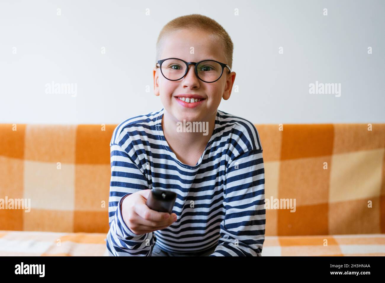 Ein Teenager schaut fernsehen und wechselt mit der Fernbedienung die Sender. Der junge Mann ist unzufrieden mit dem, was er auf dem fernsehbildschirm sieht. Sitzen auf dem Sofa im Wohnzimmer zu Hause in legerer Kleidung Stockfoto