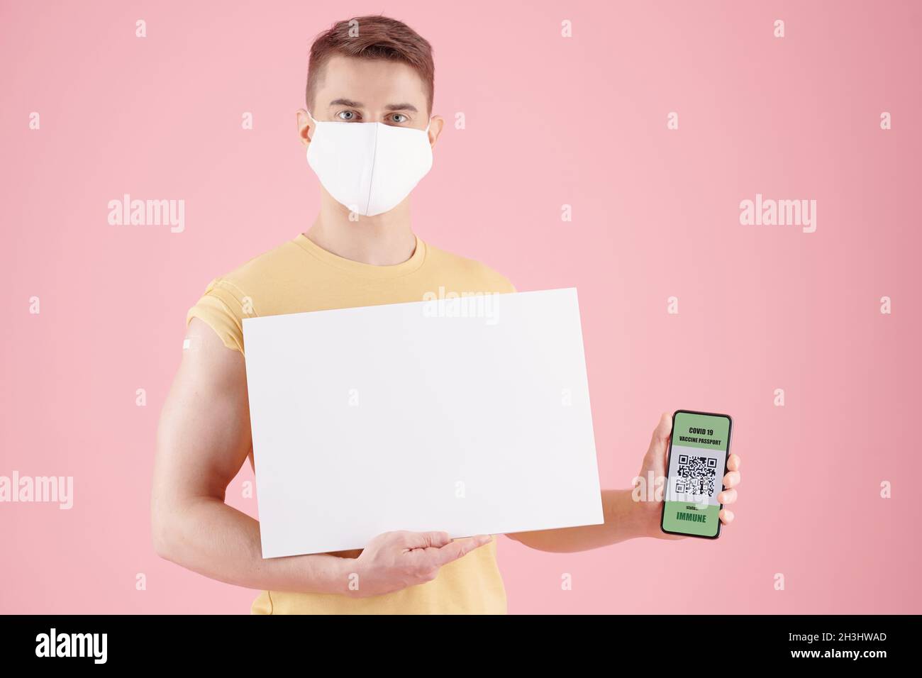 Seriöser junger Mann in Schutzmaske mit schwarzem Plakat und Smartphone mit QR-Code und Impfpass Stockfoto